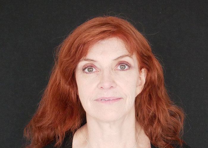 Middle-aged woman with red hair and green eyes looking directly at the camera against a black background. Saxon MD
