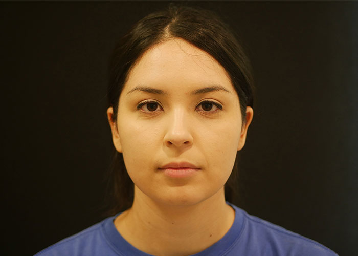 Portrait of a woman with medium-length dark hair wearing a blue shirt, facing directly towards the camera against a black background. Saxon MD